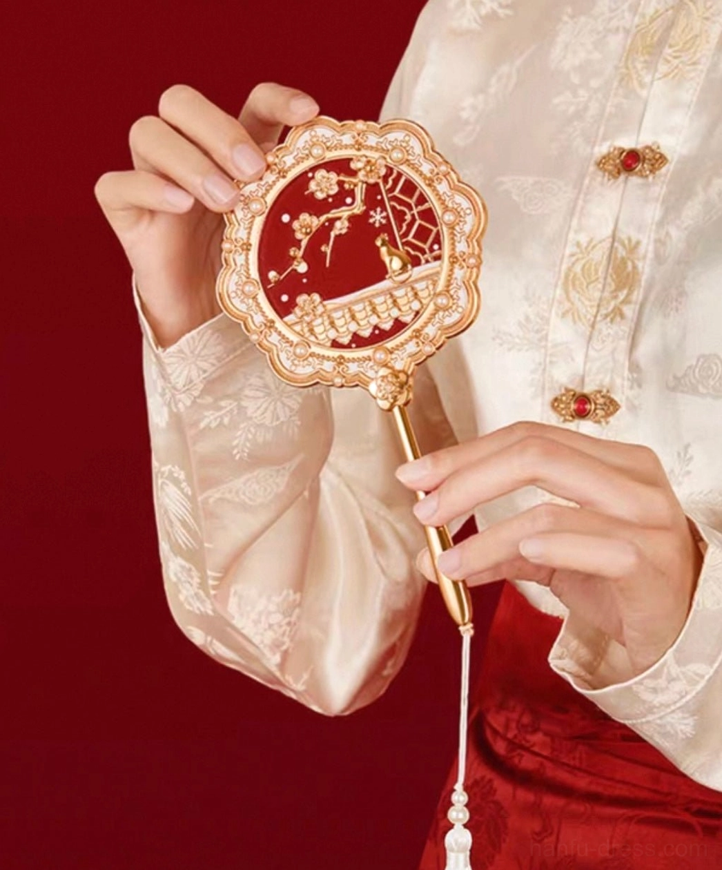 Chinese hand mirror with plum blossom cat garden design held with traditional Hanfu clothing, showing the white beaded tassel and elegant gold-toned handle
