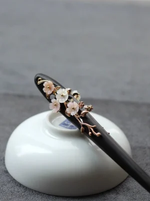 Plum blossom Chinese hair stick with dark wooden pin, rose-gold-tone branches, and pink white floral details on gray fabric