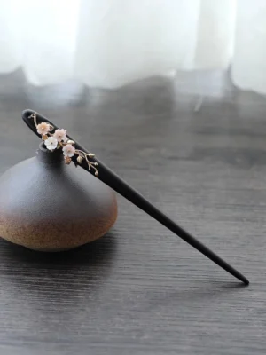Side view of a traditional Chinese dark wood hair stick with delicate plum blossom branch ornament