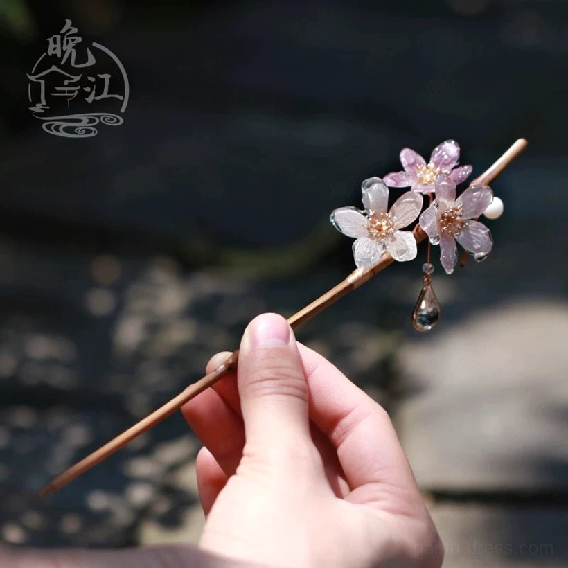 Handheld Polar Night cherry blossom Chinese hair stick showing the wood-toned shaft, translucent white and lavender flowers, pearl-like bead and teardrop crystal pendant