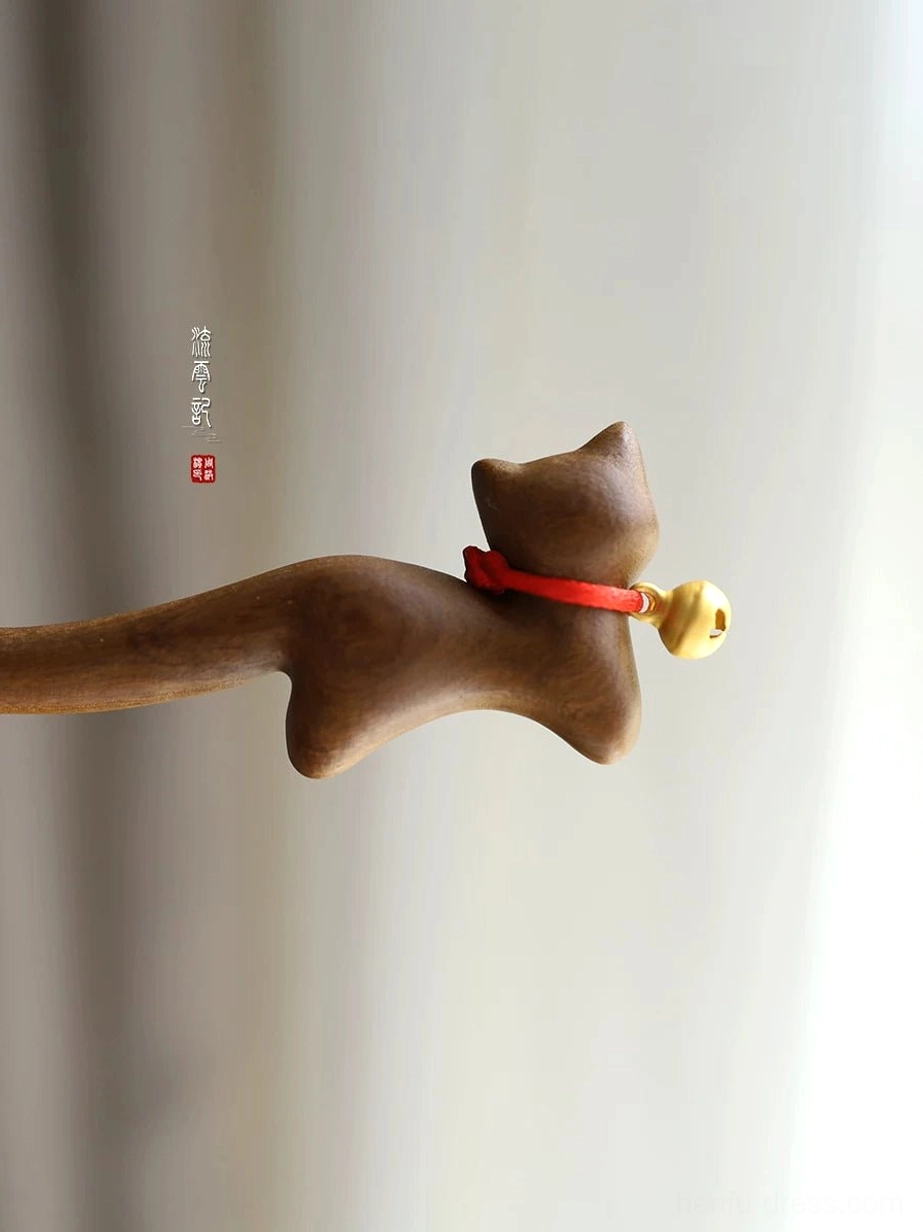 Rear side close-up of a smooth polished wooden Chinese hair stick with cat design, red collar, and shiny golden bell
