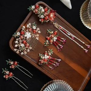 Complete pomegranate Hanfu hair accessories set with red fruit motifs, faux pearls, green leaves, floral details, gold-tone tassels, hair comb and clips displayed on a wooden tray