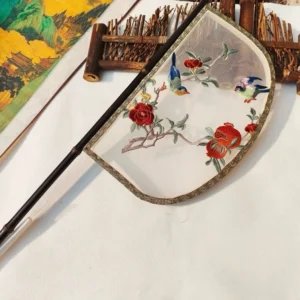 Oblique top view of an embroidered knife-shaped Chinese hand fan with a sheer silk-style fan surface, dark bamboo handle, pomegranate and songbird motifs, traditional brocade border, bamboo crafts, and Chinese landscape decor
