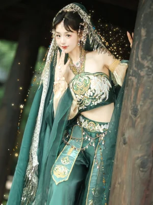 Three-quarter front view of a Dunhuang Feitian Tang Dynasty Hanfu dance costume with embroidered crop top, beige sheer lantern sleeves, beaded tulle headdress, waist ornaments, and flowing green veil in an outdoor pavilion