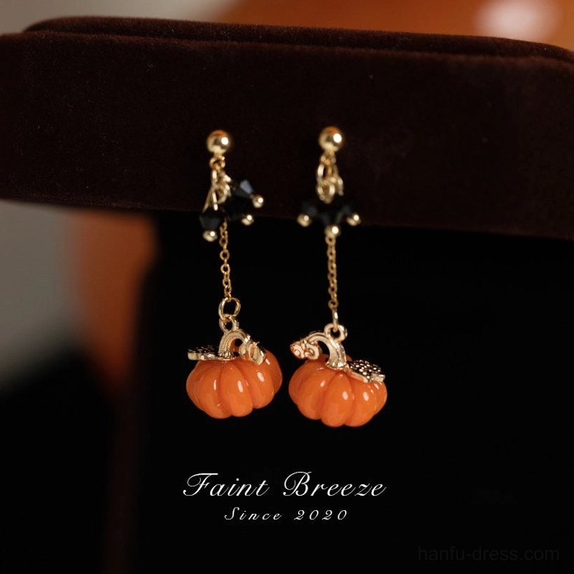 Pumpkin lantern drop stud Chinese earrings with orange ribbed pumpkin charms, gold tone chains, and black accents on a brown velvet display