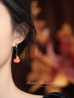 Model wearing long pumpkin lantern drop Chinese earrings with orange pumpkin pendants and gold tone chains in an autumn inspired setting
