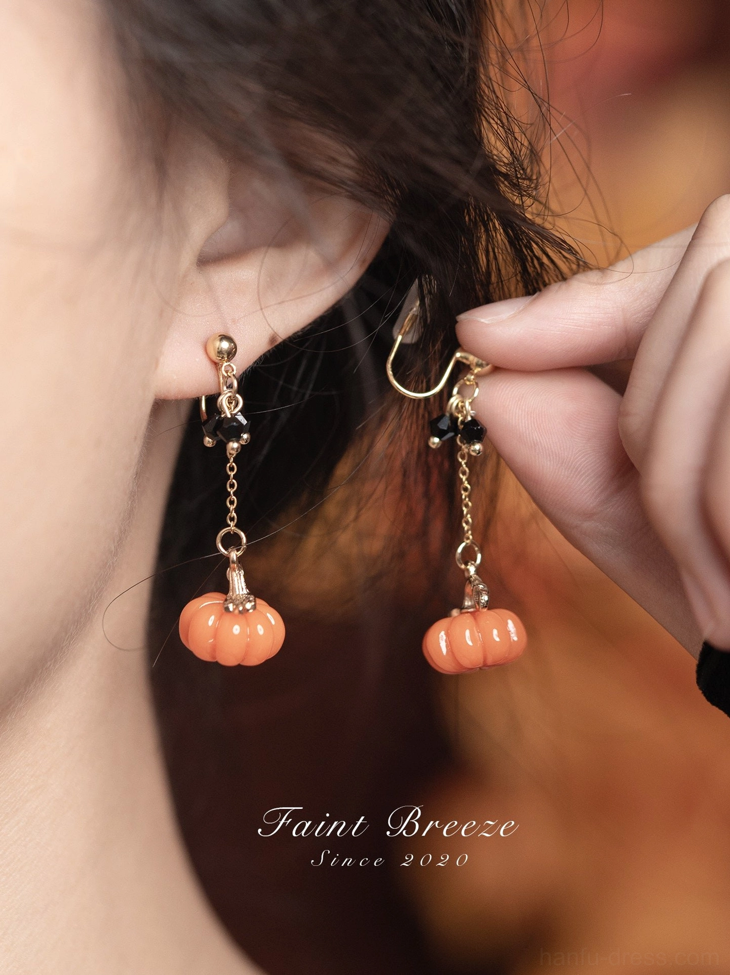 Close up of model fastening pumpkin lantern drop stud earrings with gold tone chains and orange pumpkin pendants