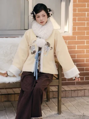 Puppet Custard modern hanfu cream yellow winter coat with dark brown wide-leg pants worn in an outdoor seated styling look