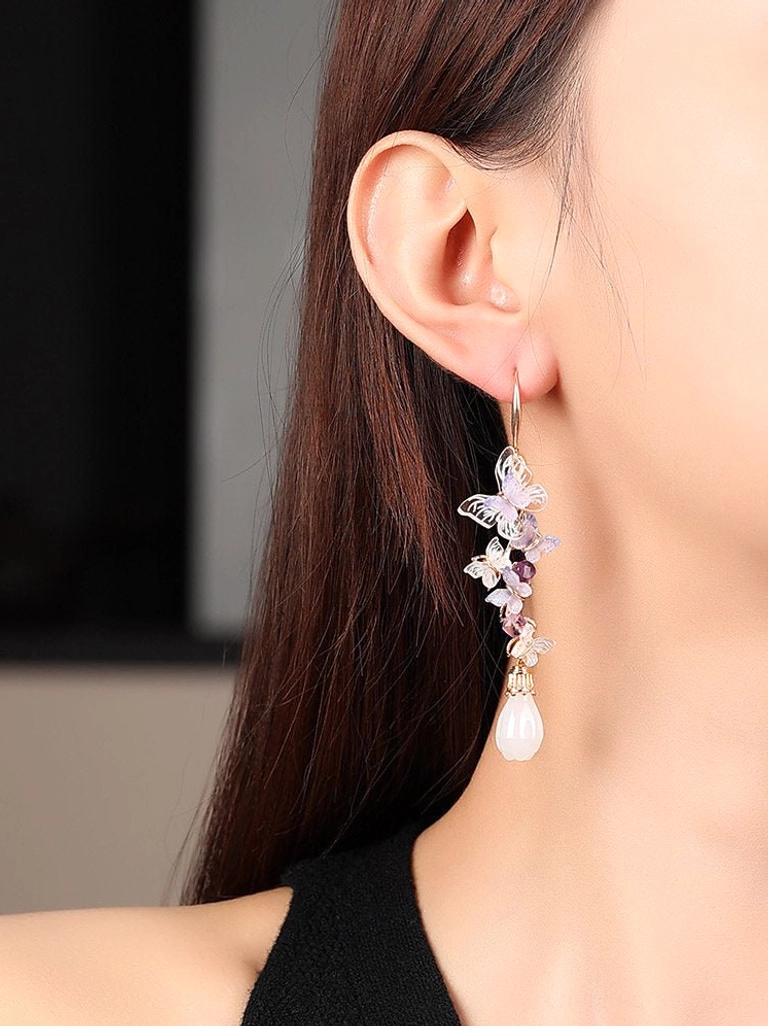 Side view of a woman wearing purple butterfly drop earrings, highlighting the butterfly bead cluster above the white teardrop pendant