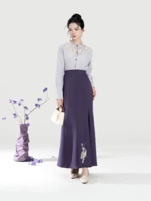 Woman wearing a purple embroidered modern Hanfu blouse and fitted mermaid skirt set with beige heels and white handbag in a studio setting
