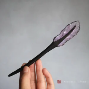 Purple feather Chinese hair stick held in hand, showing the polished black wooden shaft and translucent feather ornament