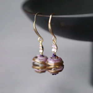 Purple floral swirl Chinese Hanfu dangle earrings with gold tone hooks, violet flower charms and spiral patterned round bead pendants displayed on a black bowl