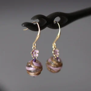 Pair of purple floral swirl Hanfu earrings with gold tone hooks, enamel style flower pendants and striped round bead drops on a dark wooden hairpin