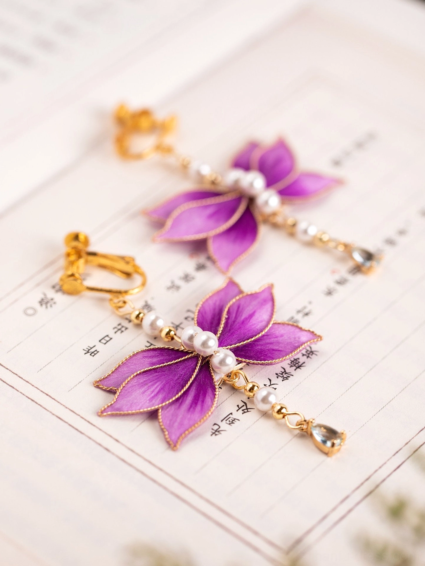 Purple flower Chinese earrings shown in hook and comfort clip-on styles with pearl centers and gold tone teardrop pendants