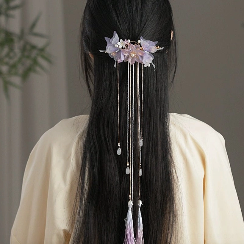Rear view of long black hair styled with a purple Hanfu hair pin and flowing tassel chains worn with a beige traditional Chinese outfit