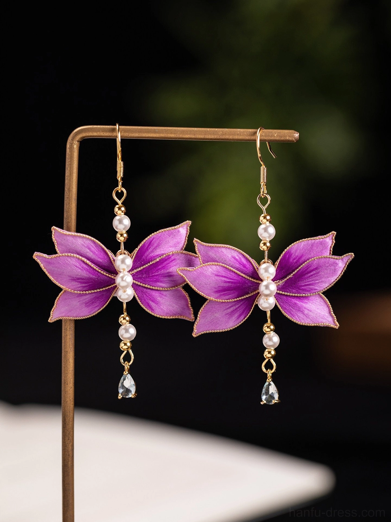 Purple lotus flower Chinese earrings hanging on jewelry stand with layered pearl centers and faceted teardrop pendants