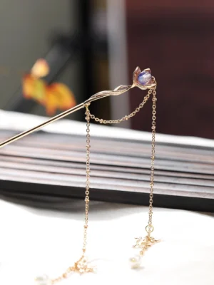 Purple lotus tassel Chinese hair stick for Hanfu shown in an overhead close-up with gold-tone pin, double chain tassels, pearl pendants, and snowflake charms