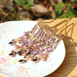 Purple pearl tassel U-shaped Chinese Hanfu hairpin with gold-tone frame, teardrop crystal pendants, and cascading chain decorations displayed on a cherry blossom ceramic plate