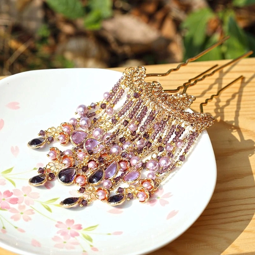 Purple pearl tassel U-shaped Chinese Hanfu hairpin with gold-tone frame, teardrop crystal pendants, and cascading chain decorations displayed on a cherry blossom ceramic plate