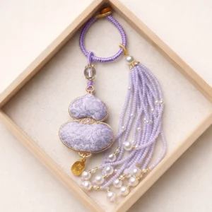 Light purple Chinese Song brocade gourd bag charm and keychain with gold-tone trim, purple beaded tassel, faux pearl accents, braided wrist strap, and decorative hanging ornament displayed in a wooden tray