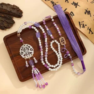 Traditional Chinese Yingluo tassel necklace displayed on a wooden tray with vintage calligraphy, featuring a hollow white longevity pendant, purple and white beads, and a long purple tassel