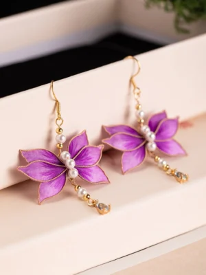 Purple velvet lotus flower Chinese earrings with pearl centers and gold tone teardrop dangles displayed on a light gift tray