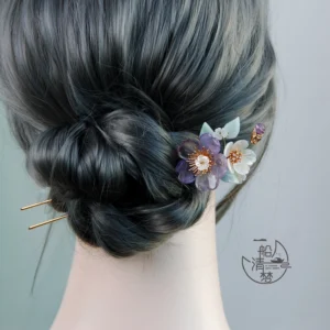 Traditional Chinese floral hair stick arranged in a dark low chignon with purple and white flowers and gold double-pronged hair ornament