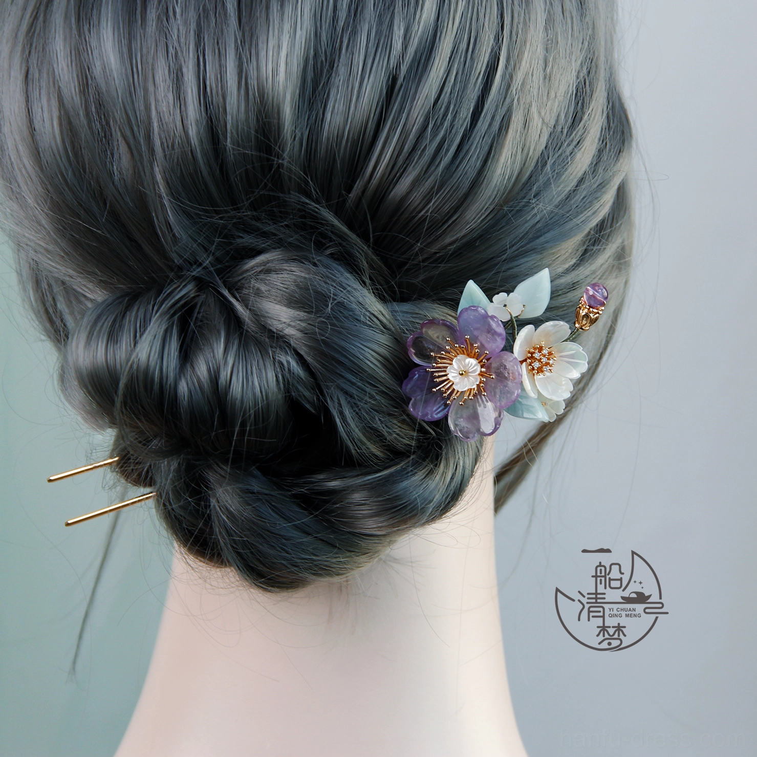 Traditional Chinese floral hair stick arranged in a dark low chignon with purple and white flowers and gold double-pronged hair ornament