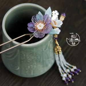 Purple and white traditional Chinese flower hair stick with light blue leaves displayed on a carved celadon ceramic cup