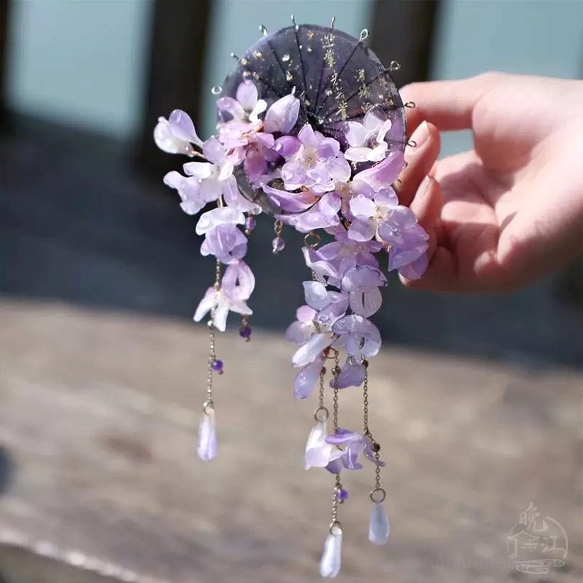 Side view of purple wisteria Chinese hair stick accessory with layered violet flowers, gold-tone chains, and long clear drop pendants on wooden surface