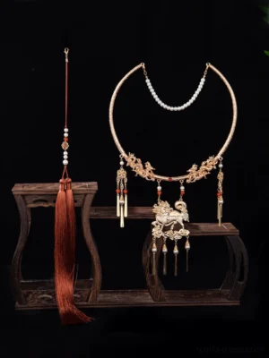 Front view of a traditional Qilin Chinese necklace with carved gold-tone dragon collar, pearl front chain, red bead accents, mythical Qilin pendant, and decorative back tassels displayed on a vintage wooden stand