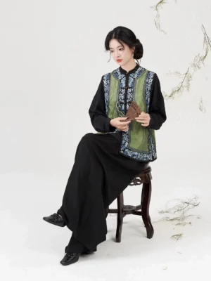Qing Dynasty inspired embroidered jacquard vest shown from the side while seated, highlighting the flowing silhouette and layered styling