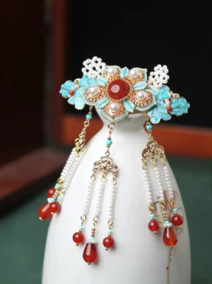 Traditional Chinese tassel hair pin with turquoise enamel floral frame, red agate accents, faux pearls, and layered beaded pendants displayed on a ceramic stand
