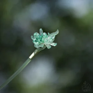 Qingyuan green chrysanthemum Chinese hair stick with translucent layered floral head displayed against a soft outdoor green background