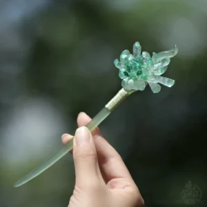 Hand holding Qingyuan green chrysanthemum Chinese hair stick showing the layered translucent flower and jade-style pin