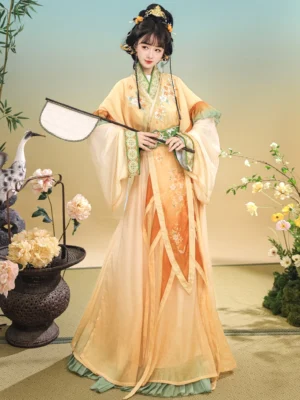 Front full-body view of Qiuxiang Wei Jin Dynasty Qiyao Ruqun Hanfu with yellow-orange gradient fabric, floral embroidery, green layered trims, wide sleeves, and flowing chiffon skirt in an oriental studio