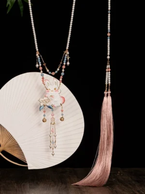 Rabbit lotus yingluo Chinese necklace with pastel pink and blue beads, pearl details, tassel, and dangling charms displayed beside a round fan
