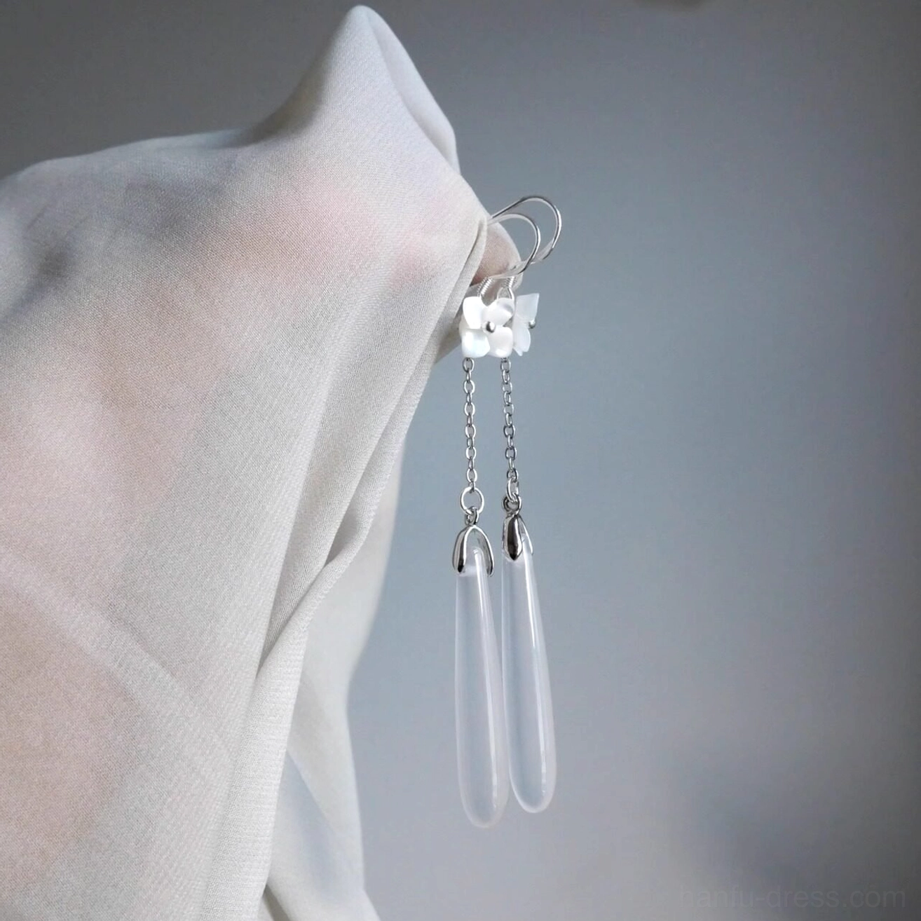 Close-up side view of white flower Hanfu earrings with polished silver-tone hardware and clear translucent teardrop pendants on sheer fabric