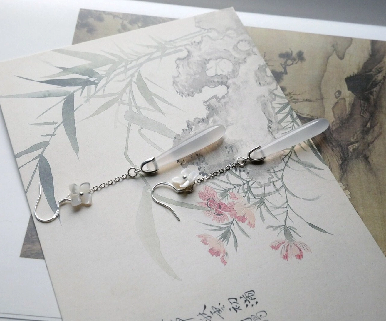 White flower long drop Hanfu earrings displayed on Chinese ink painting postcards with silver-tone chains and smooth translucent teardrop pendants