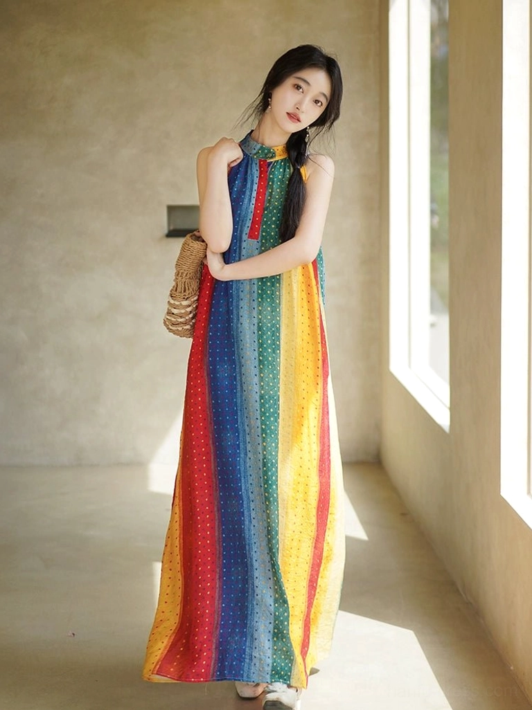 Three-quarter front view of a woman wearing a rainbow modern Hanfu halter maxi dress with vertical striped polka dot print, sleeveless stand collar, red front placket trim, and flowing floor-length silhouette in a vintage indoor corridor