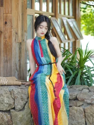 Modern rainbow Hanfu-inspired maxi dress with black waist belt, colorful vertical stripes and tiny polka dots, sleeveless halter collar, and flowing floor-length fit styled beside a stone terrace