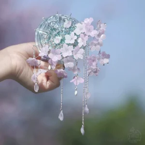 Raining cherry blossoms Chinese hair stick with pink and purple flower clusters silver tassels and teardrop pendants held against a soft outdoor blossom background