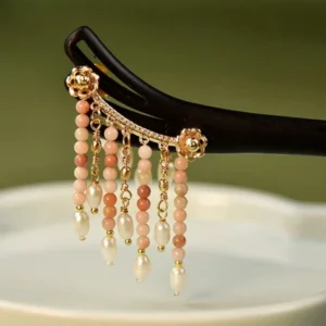 Traditional Chinese wooden tassel hairpin displayed on a white porcelain plate with rosy brown beads, pearl drops and gold-tone floral details