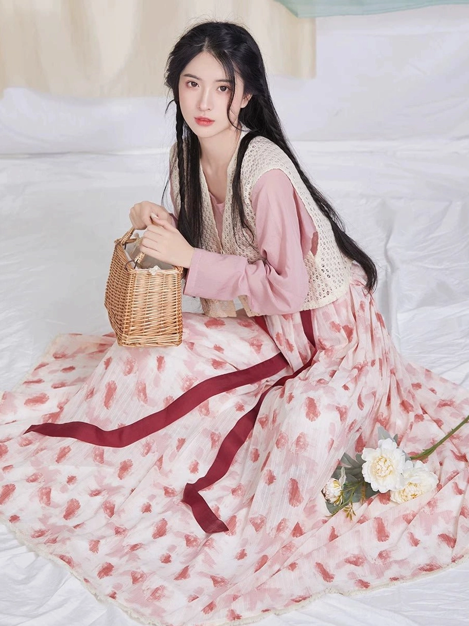 Overhead seated styling of a raspberry-print hanfu pleated skirt spread in a circle with the layered Tang-inspired outfit and floral props