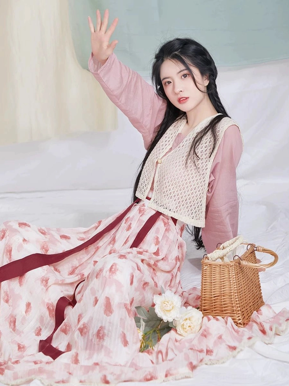 Front seated portrait in a modern Tang Dynasty hanfu set with raspberry-print pleated skirt, pink top, crochet vest, and coordinating accessories