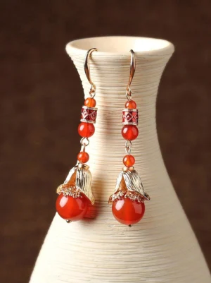 Red agate Chinese dangling earrings displayed on a beige ceramic vase with gold floral bead caps and enamel decorative spacers
