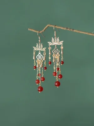 Pair of red agate lotus tassel Chinese earrings hanging from a natural branch, showing antique gold-tone metal details and symmetrical traditional Hanfu jewelry design