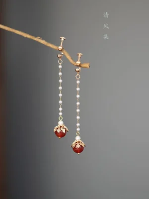 Non-pierced red agate Chinese ear clip earrings with gold floral pendants and matching decorative chains shown against a dark gray background