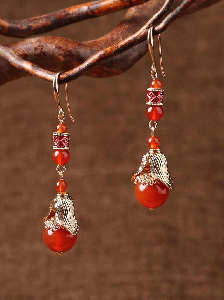 Close-up of vintage red agate cheongsam earrings hanging from a branch, showing layered beads and ornate gold-tone details