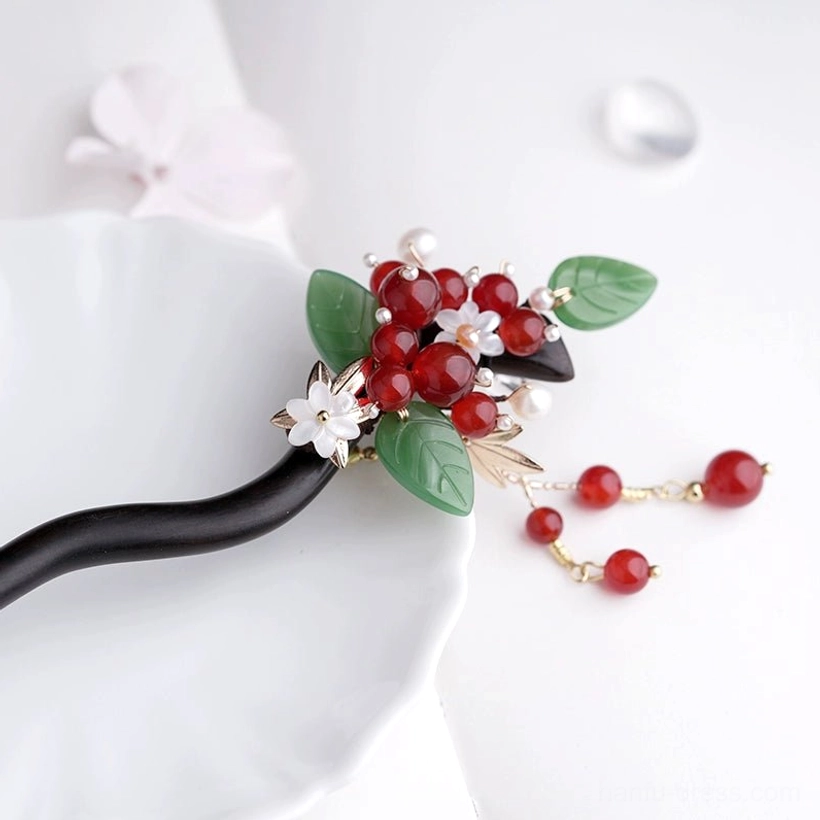 Close-up side view of red bean Chinese hairpin showing detachable red bead tassel, gold chains, white flower, and green leaf decorations